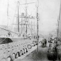 Le déchargement d’une cargaison de mélasse en fût des Antilles à partir du brick Boston Marine, sur un quai de Baltimore, Maryland, circa 1900.